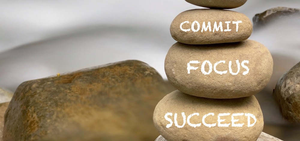 Inspirational and motivational words of decide, commit, focus, succeed on stones with blurred rushing water background